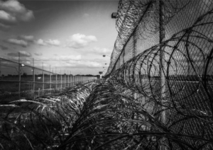Czarno białe zdjęcie z drutem kolczastym na ogrodzeniu terenu więziennego