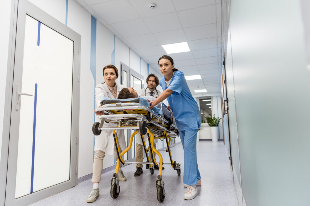 Troje lekarzy dwie kobiety i jeden mężczyzna wiozą pacjenta na łóżku przez korytarz szpitalny.