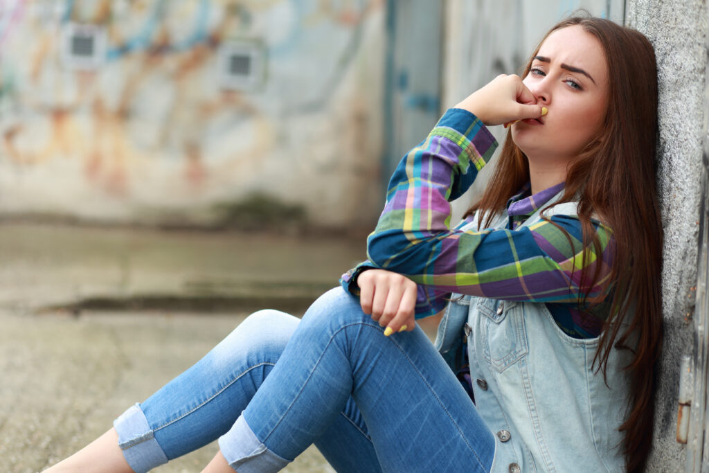 Smutna długowłosa nastolatka siedzi na ziemi przy ścianie.